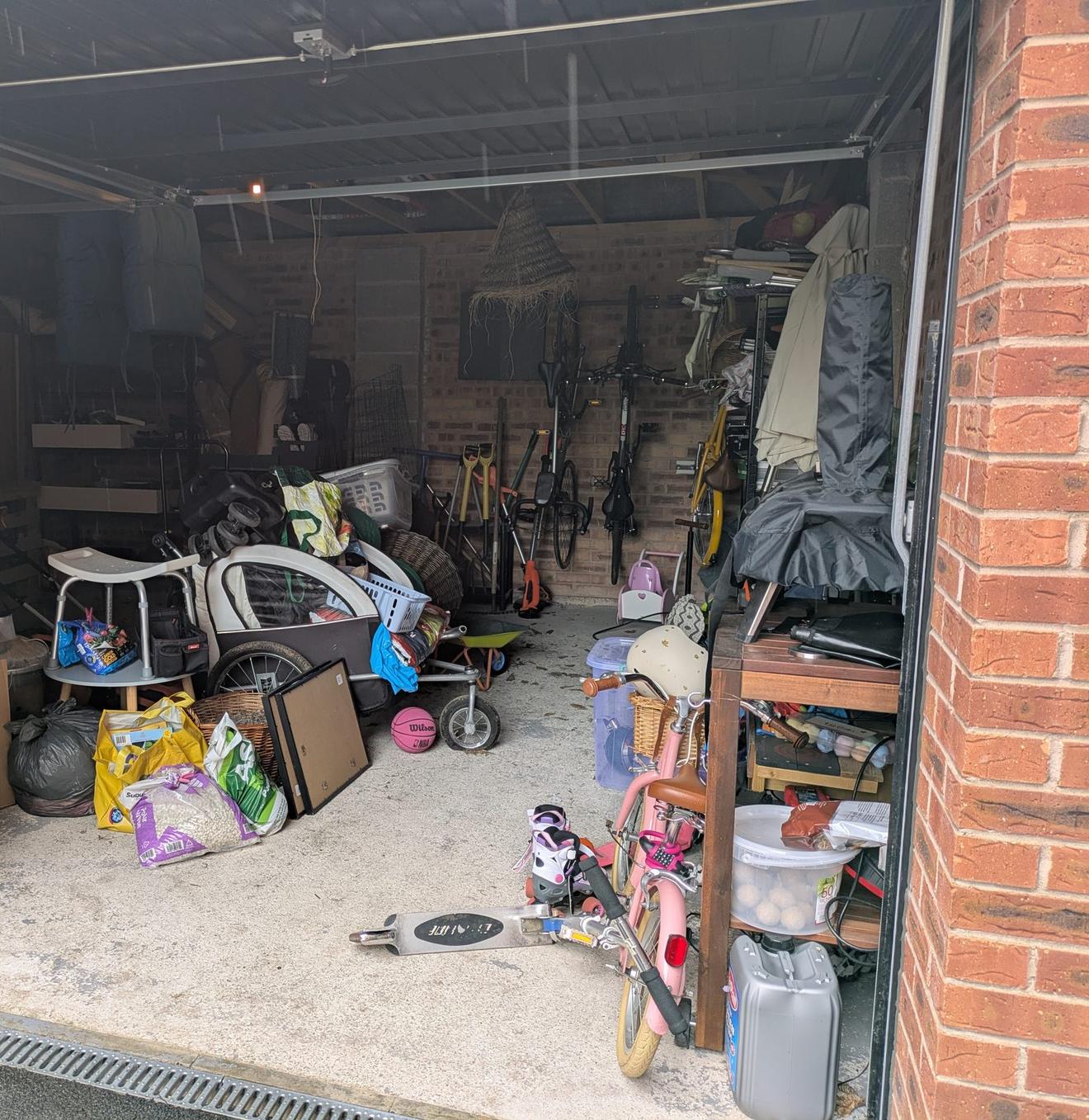 A garage crammed with family clutter: bikes, a pram, tools, boxes, bags and children's toys