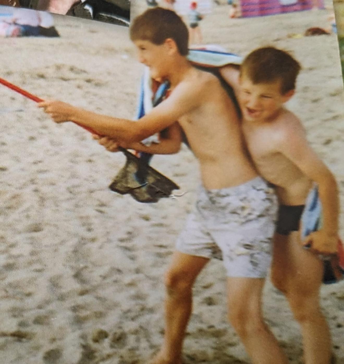 An old photograph of two young brothers on a beach at Shell Island, one holding a fishing net, both laughing