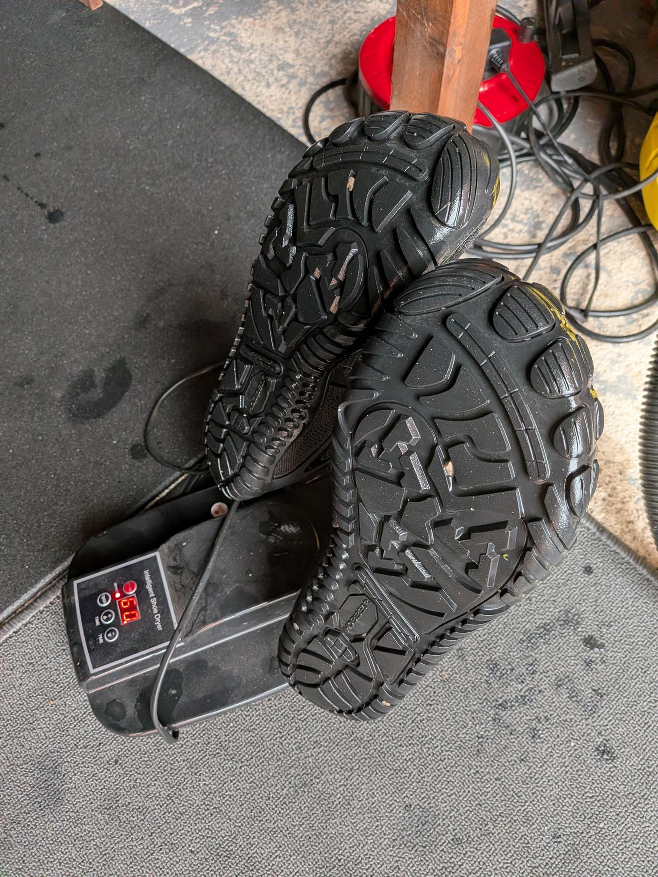 A pair of soaked trail shoes propped on an electric shoe dryer in the garage