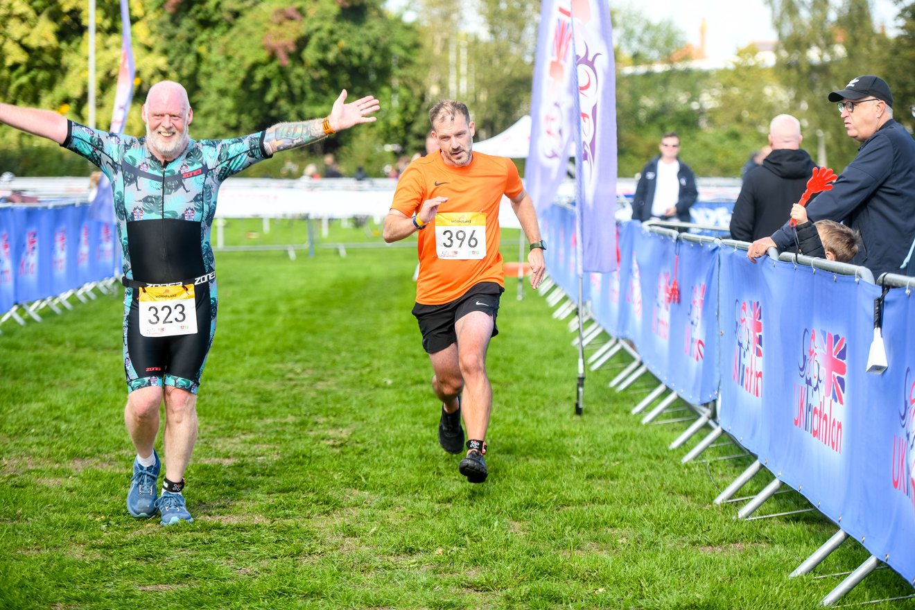 Overtaking another runner with his arms out celebrating, close to the finish chute