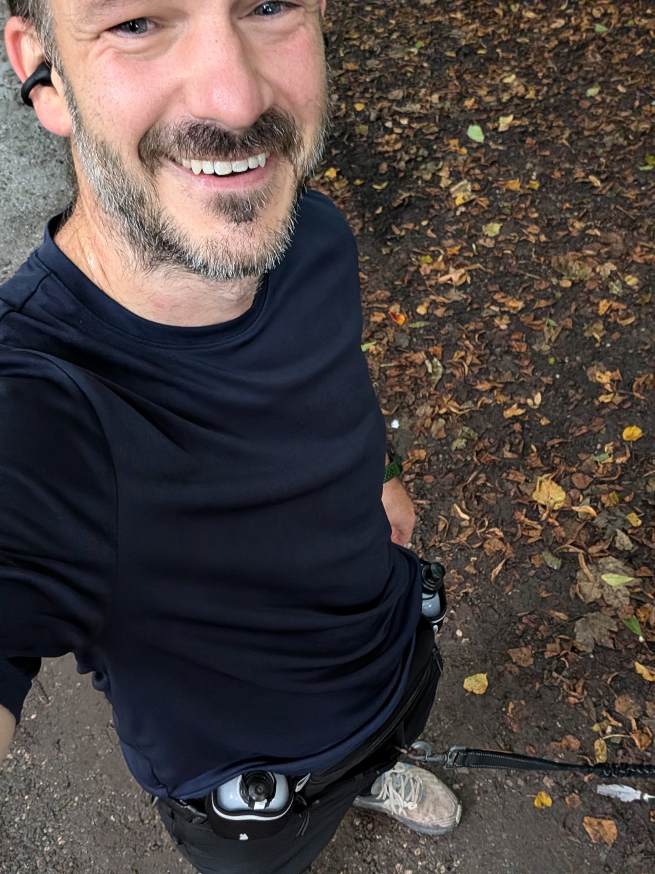 Selfie sheltering under a tree by the river, running belt on, rain-soaked leaves on the ground